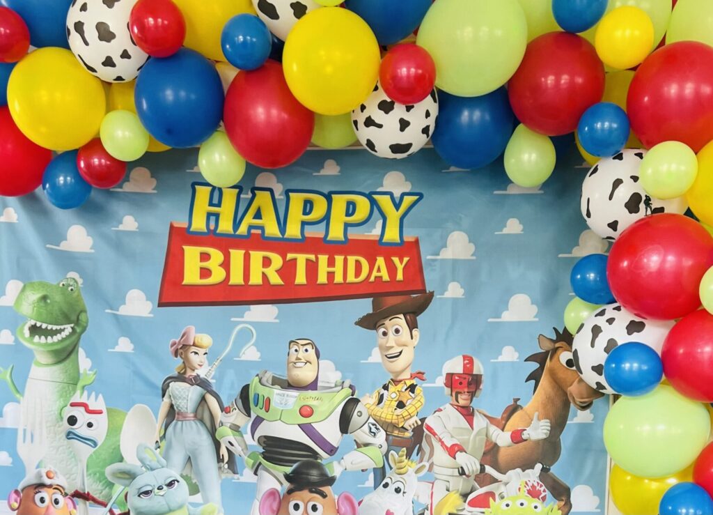 Toy Story happy birthday backdrop picturing several Toy Story characters and a multicolor balloon garland