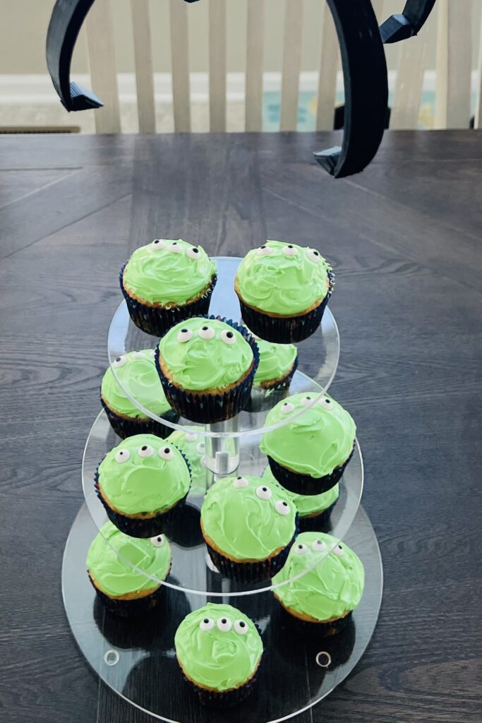 Green frosted cupcakes with three eyeball sprinkles displayed on a tiered cupcake stand