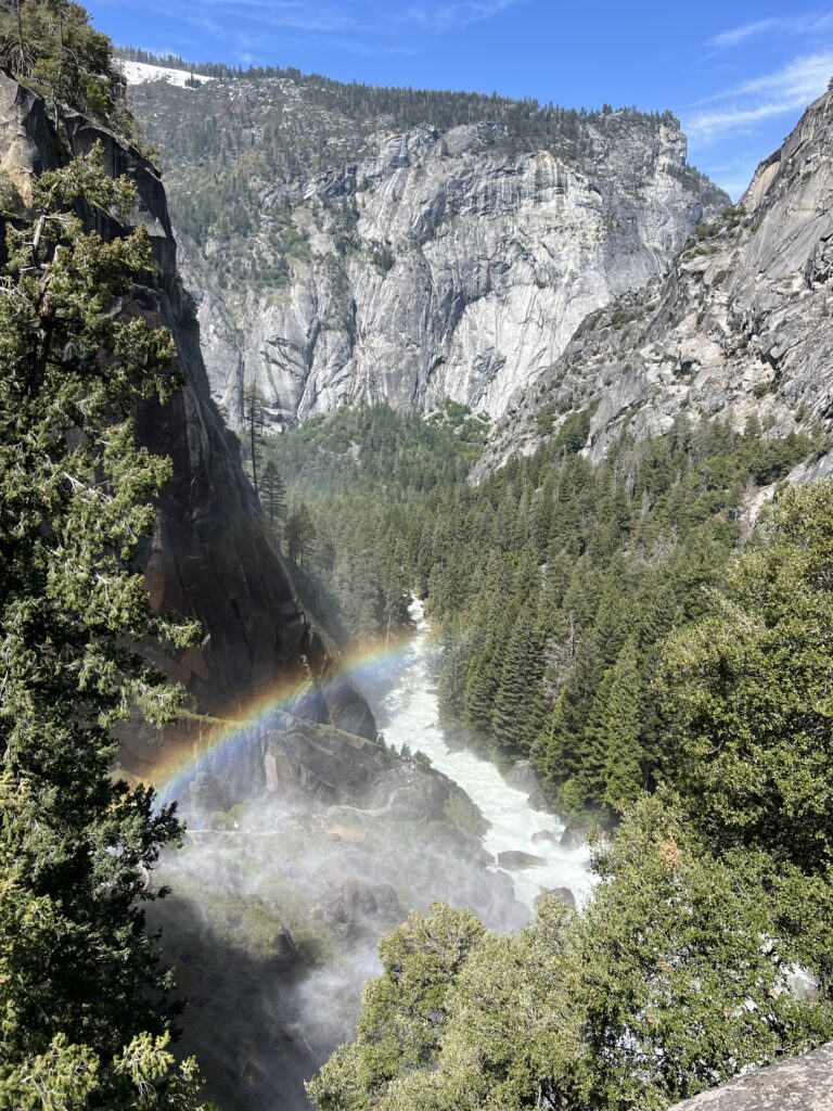 Rainbow over the Merced River surrounded by mountains and trees in Yosemite National Park